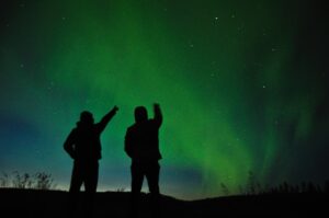 two silhouettes pointing at Tromso northern lights in sky